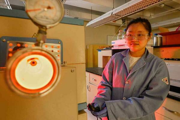 A female student operates an incinerator used for Per- and polyfluoroalkyl substances (PFAS) research in the Kyle Doudrick lab. The incinerator glows red with heat.