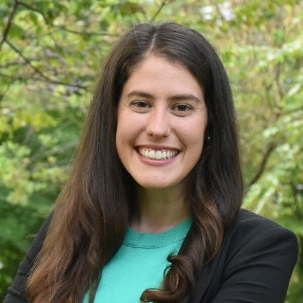 Woman in teal shirt and black blazer outdoors.